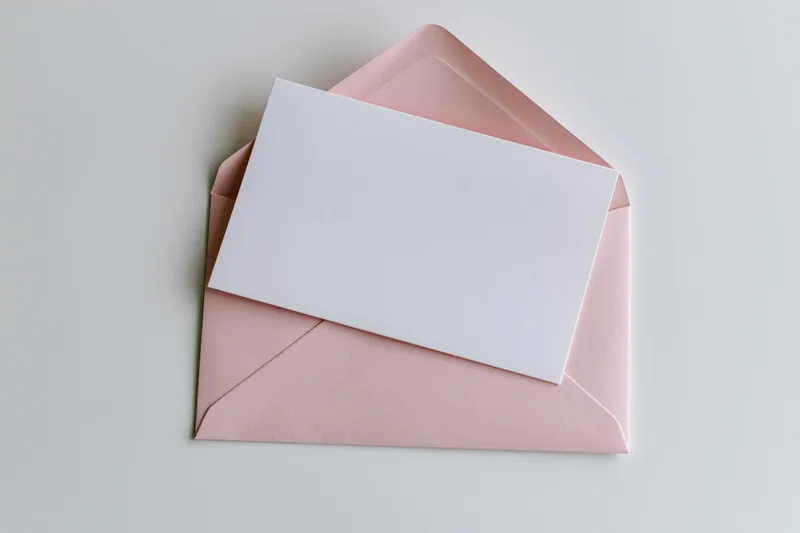 Blank white card resting on open pink envelope on light surface