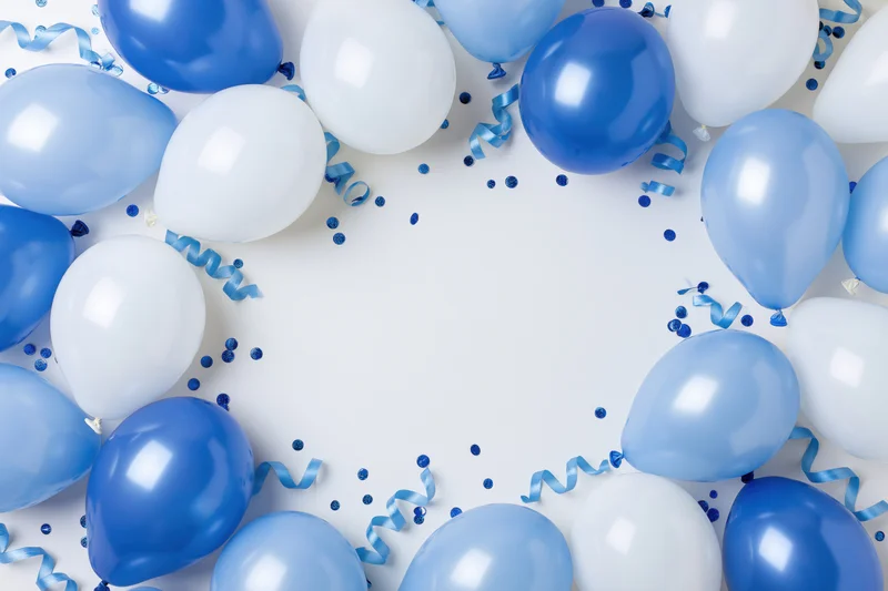 Blue and white helium balloons arranged in a circular border with confetti and streamers on white background