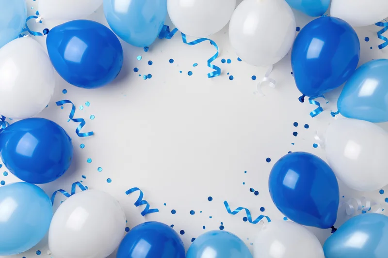 Blue and white helium balloons arranged in a circular border with confetti and streamers on a white surface