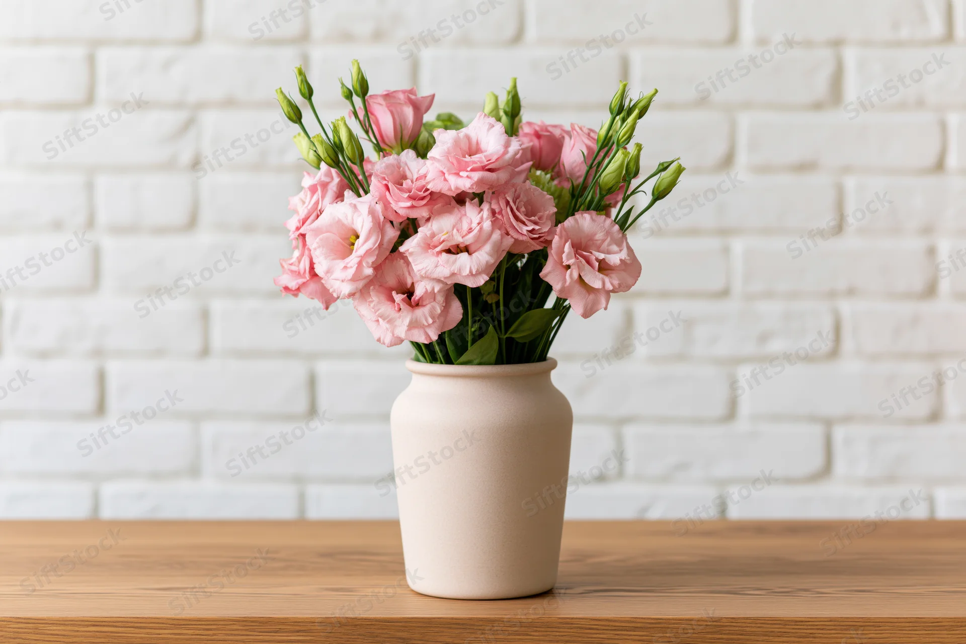 Pink lisianthus bouquet in a ceramic vase on a wooden table against a white brick wall