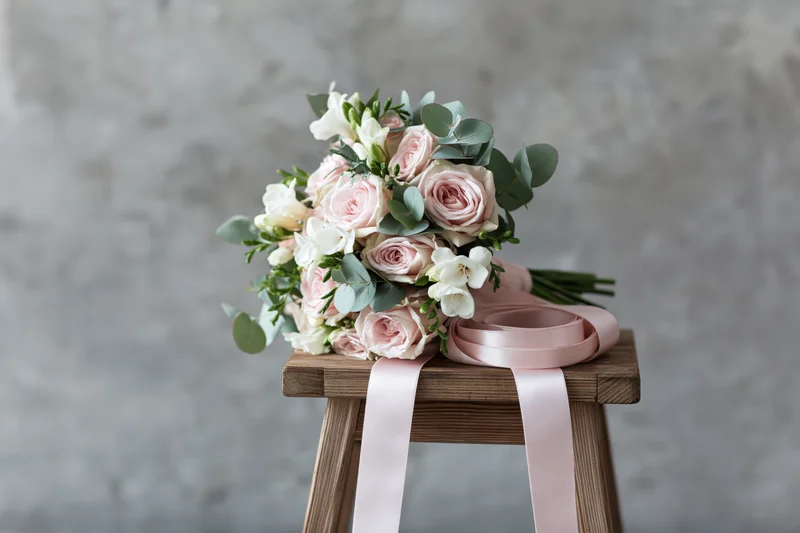 Bridal bouquet of blush pink roses and white freesia with green eucalyptus on a wooden stool