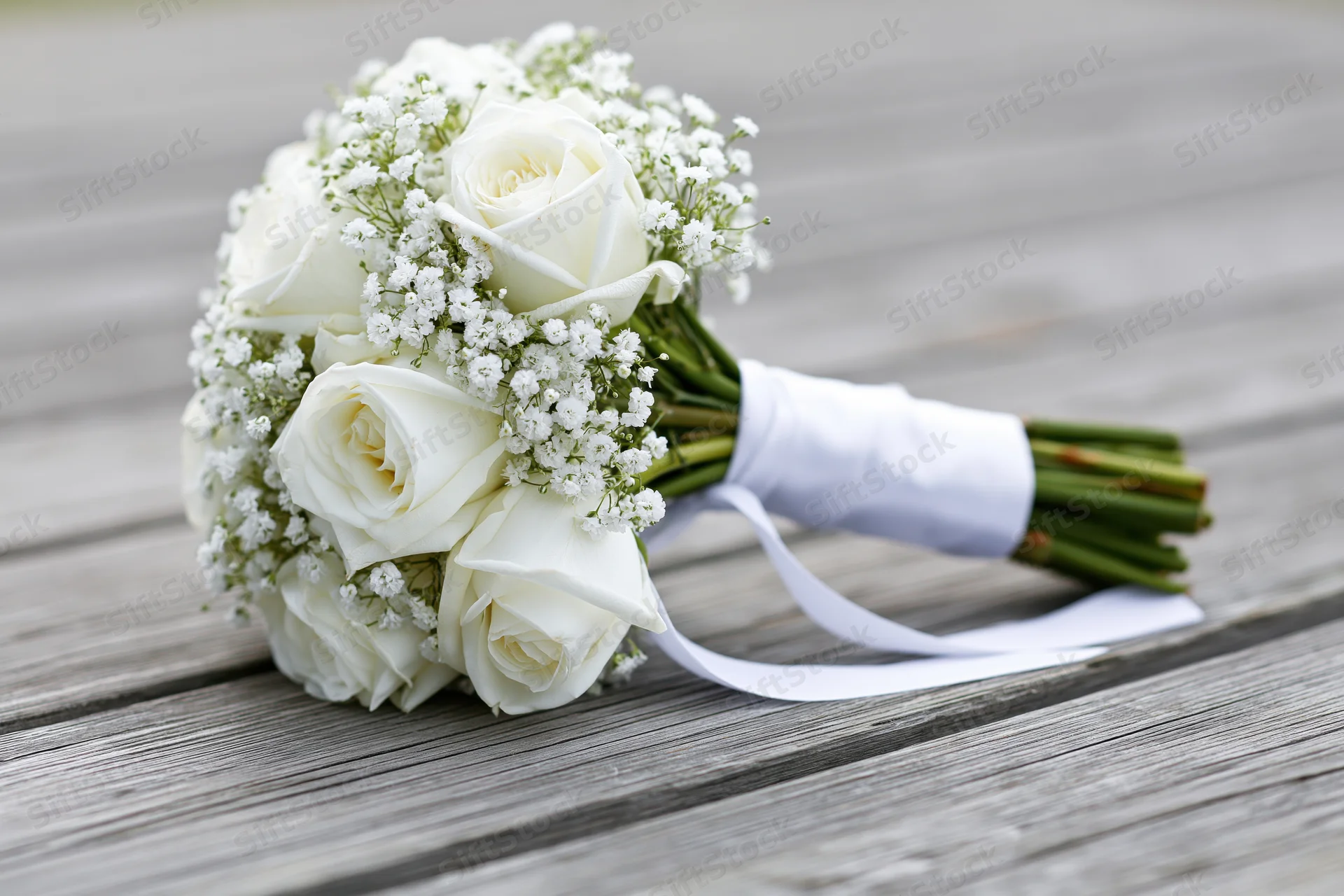 Bridal bouquet of white roses and baby's breath resting on weathered wooden deck
