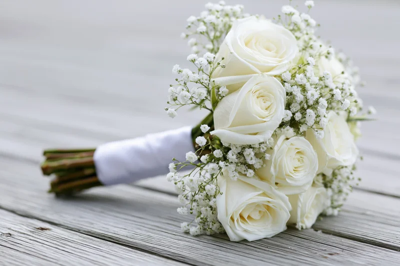 Bridal bouquet of white roses and baby's breath resting on weathered wooden surface