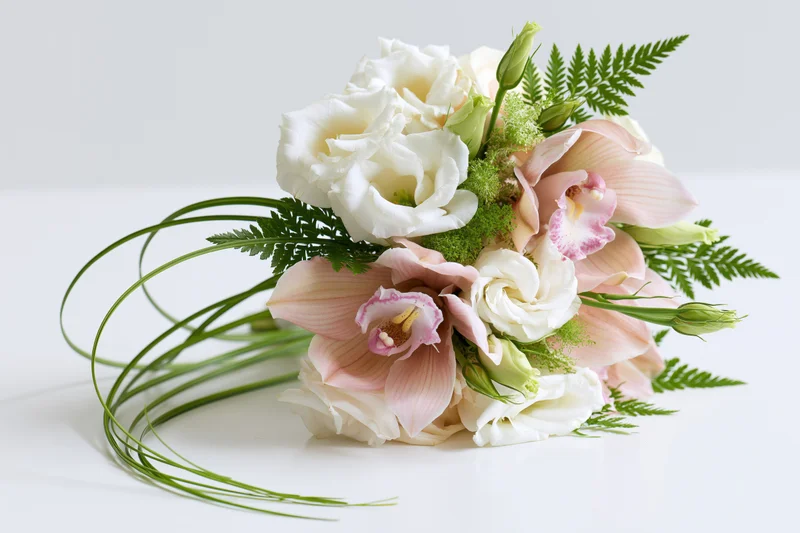Bridal bouquet with white roses and pink orchids arranged with green ferns and stems on a white surface