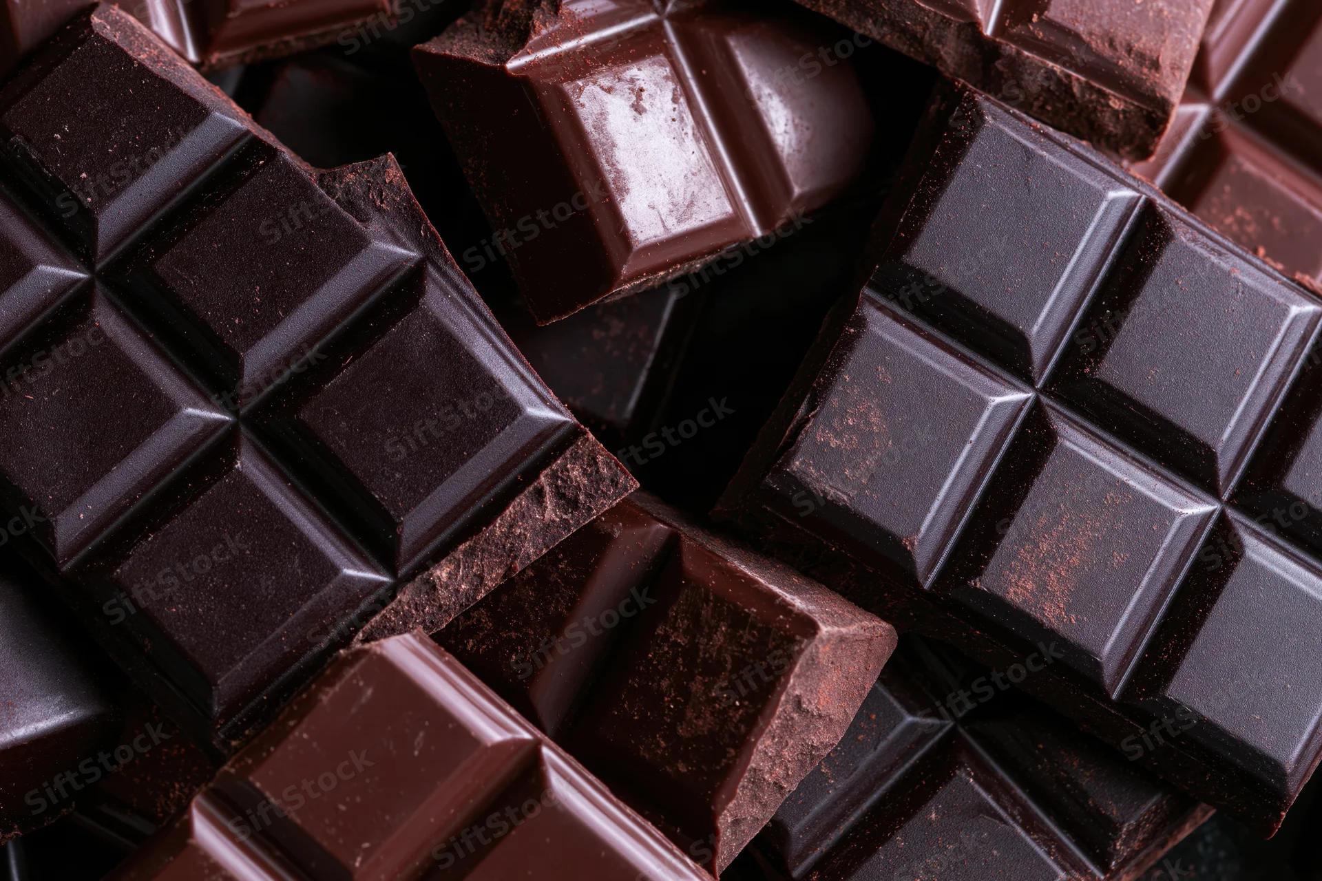 Broken dark chocolate bars scattered and stacked in closeup view