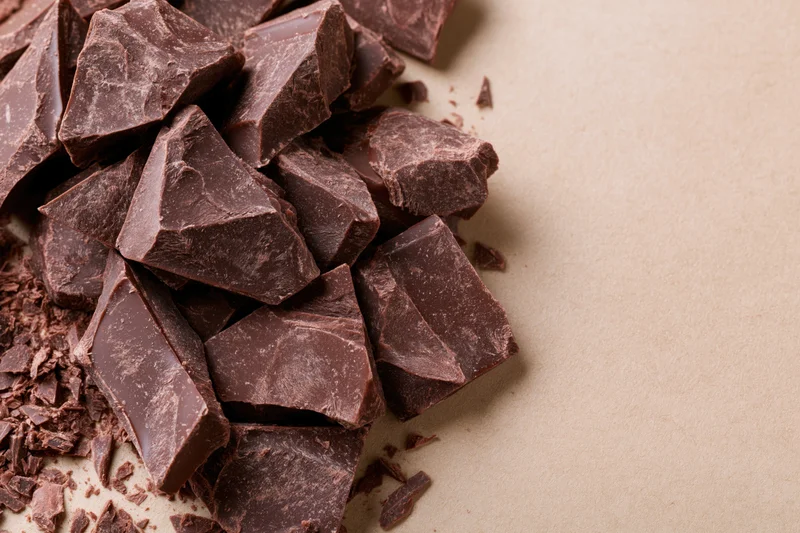 Broken dark chocolate chunks piled loosely on beige paper surface