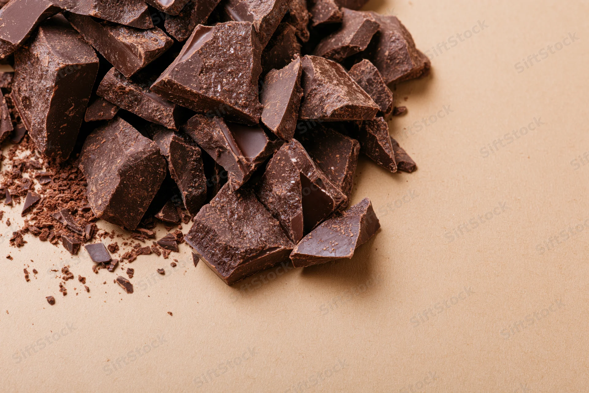 Broken dark chocolate chunks piled loosely on brown paper with copyspace