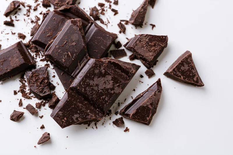 Broken dark chocolate pieces scattered on a white surface