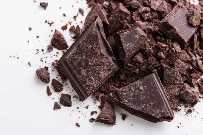 Broken dark chocolate pieces scattered on a white surface