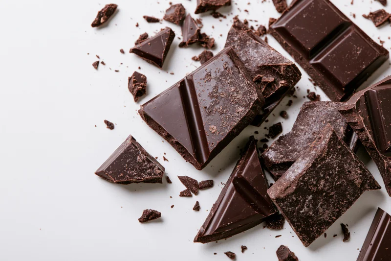 Broken dark chocolate pieces scattered across a white surface