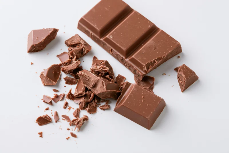 Broken milk chocolate bar with scattered pieces on white background