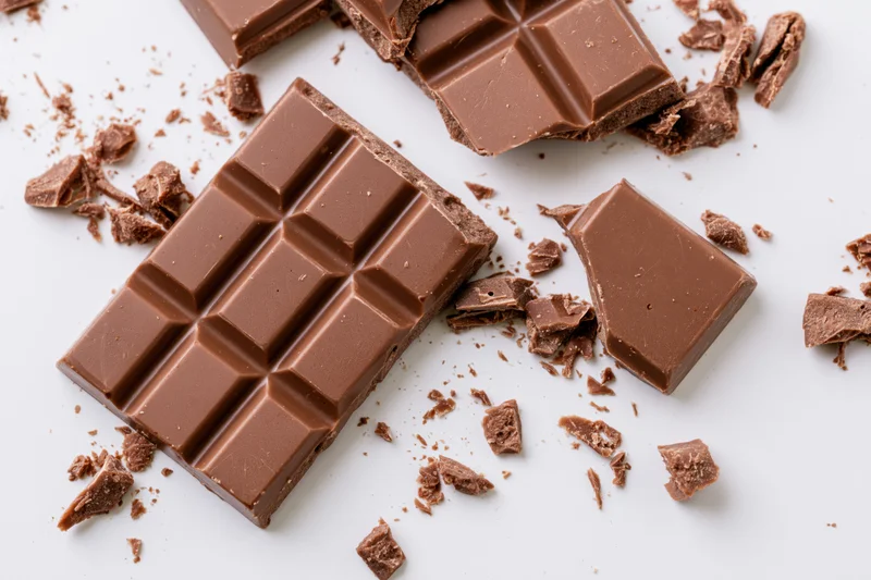Broken milk chocolate bar pieces scattered on white surface