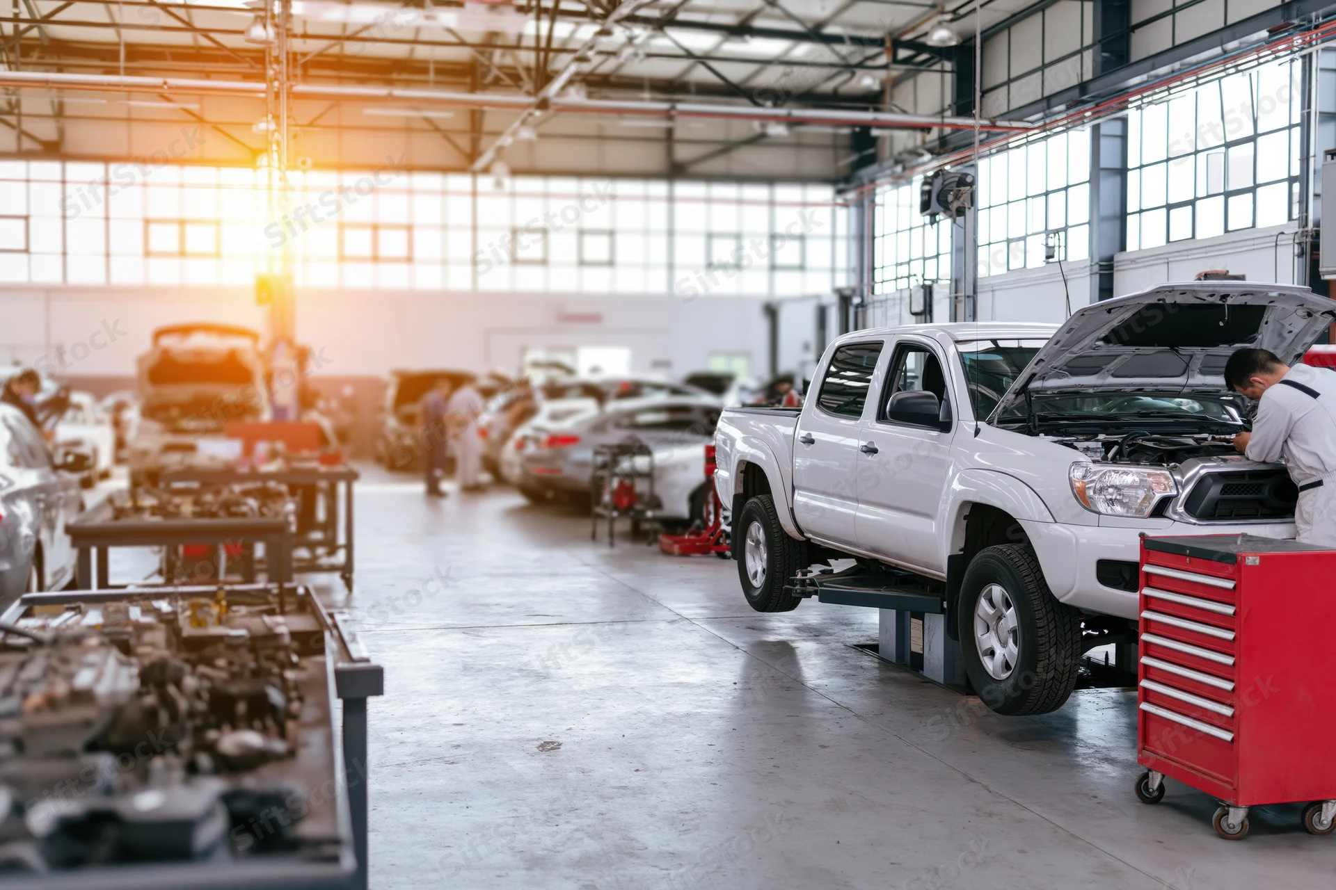 Mechanic working under open hood of white pickup truck in automotive repair shop