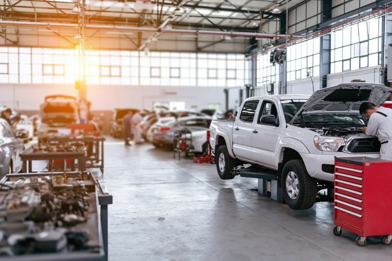 Mechanic working under open hood of white pickup truck in automotive repair shop