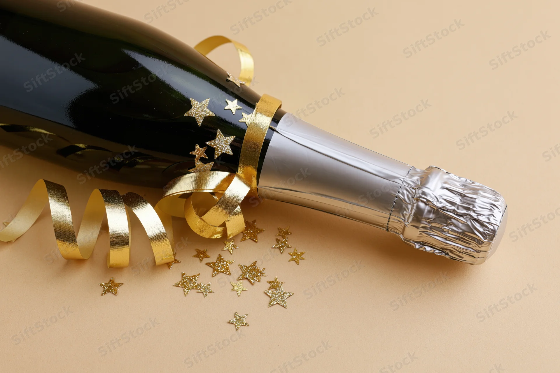 Champagne bottle decorated with gold ribbon and star confetti lying on beige surface