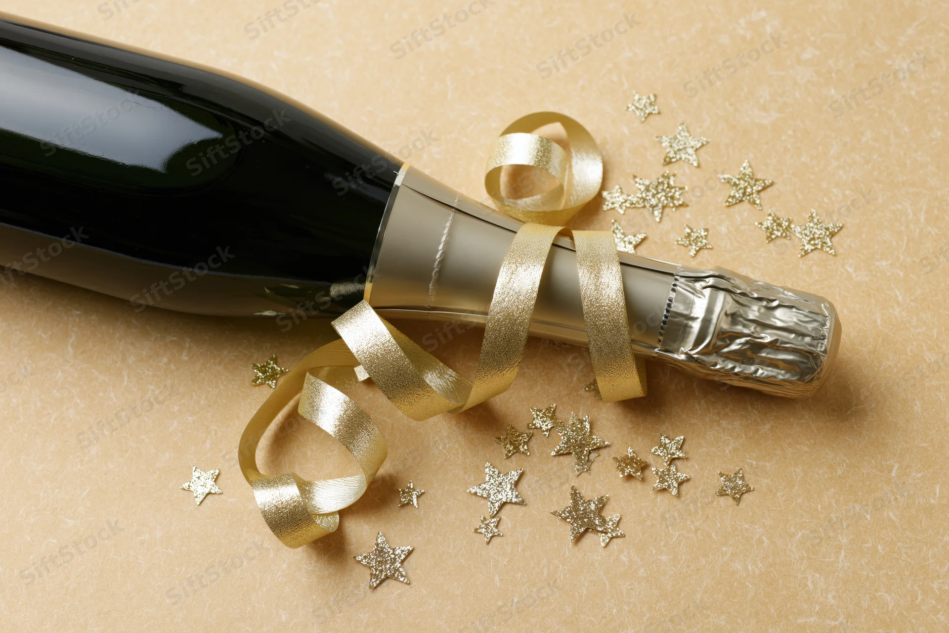 Champagne bottle lying on its side with gold ribbon and star confetti on textured surface