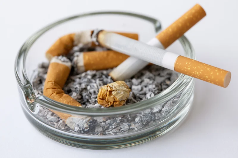 Clear glass ashtray filled with cigarette butts and ash on white background