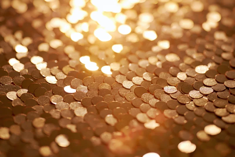 Close-up of gold sequins arranged in a flat pattern with light reflecting off their surface