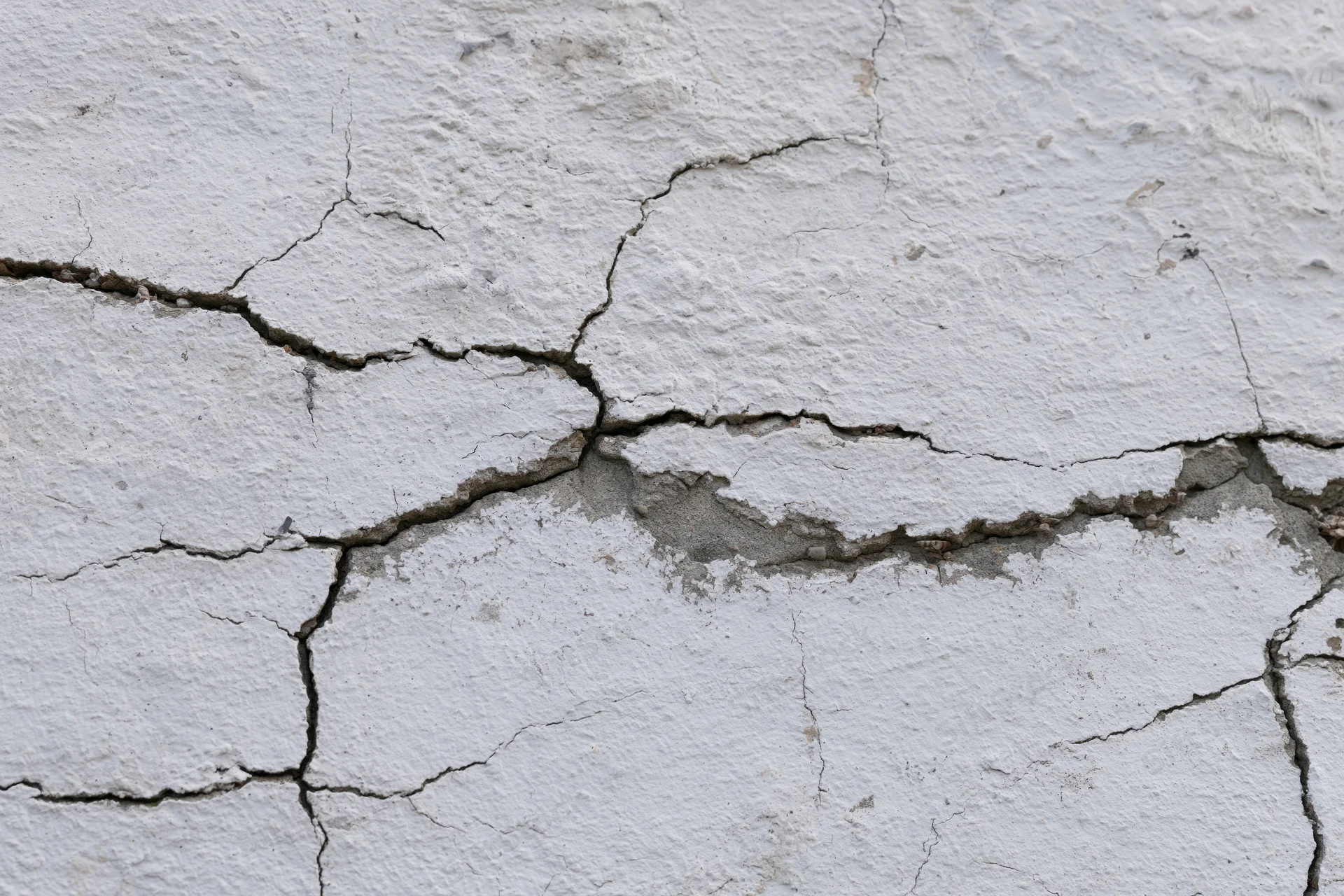 Close-up of cracked white concrete wall surface showing damage and texture