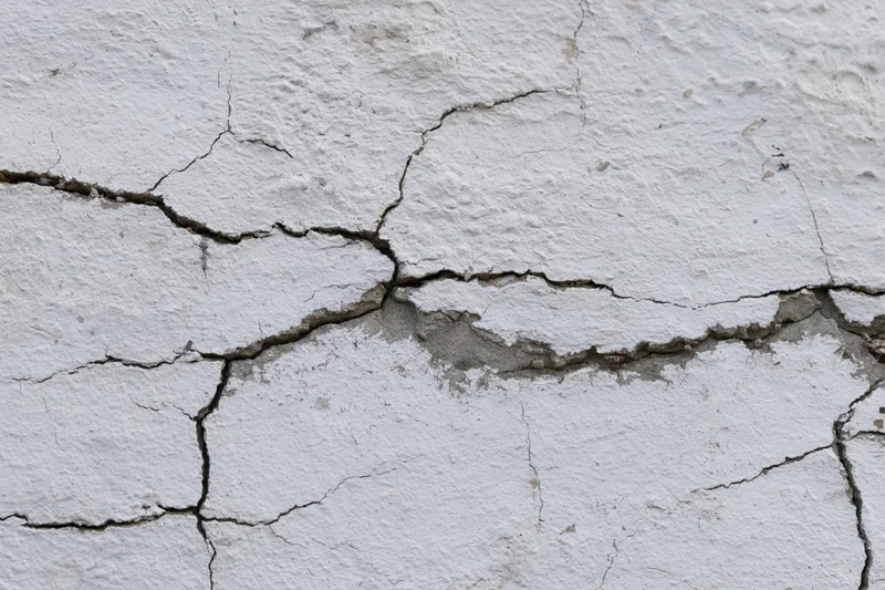 Close-up of cracked white concrete wall surface showing damage and texture