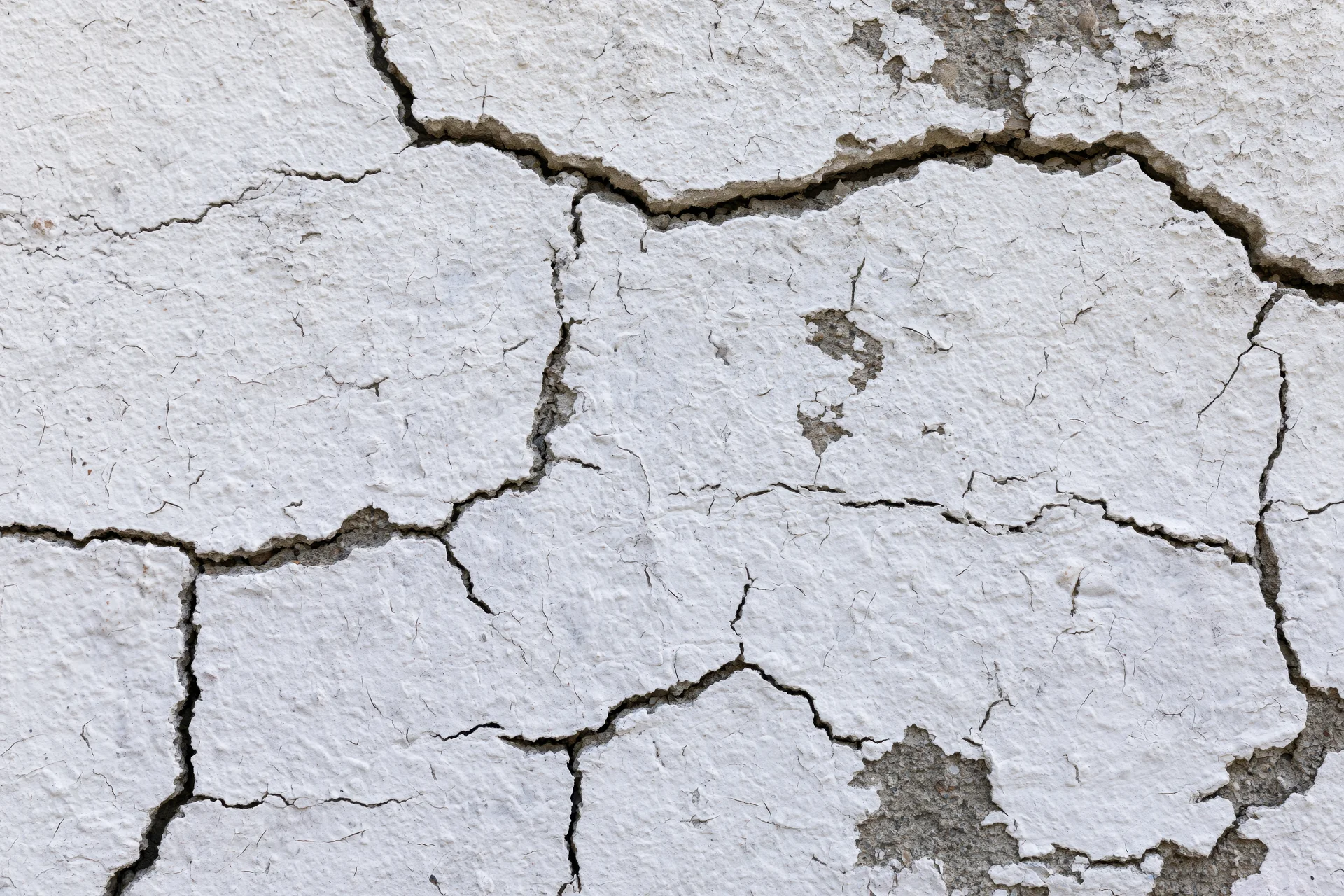 Close-up of cracked white plaster on a weathered concrete wall surface