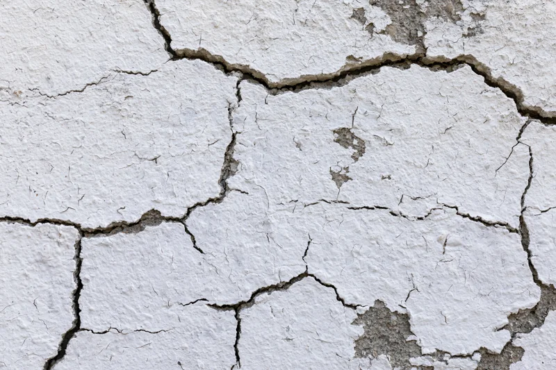 Close-up of cracked white plaster on a weathered concrete wall surface