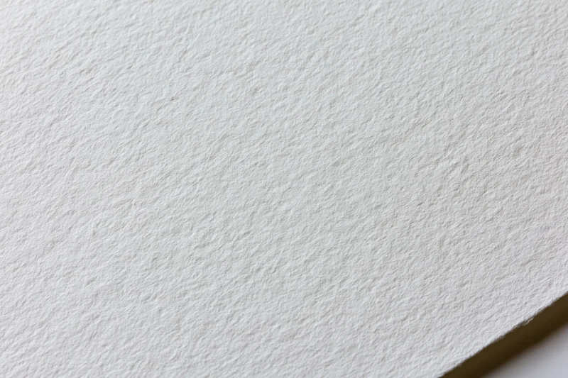 Close-up of plain white watercolor paper texture with visible grain and corner fold