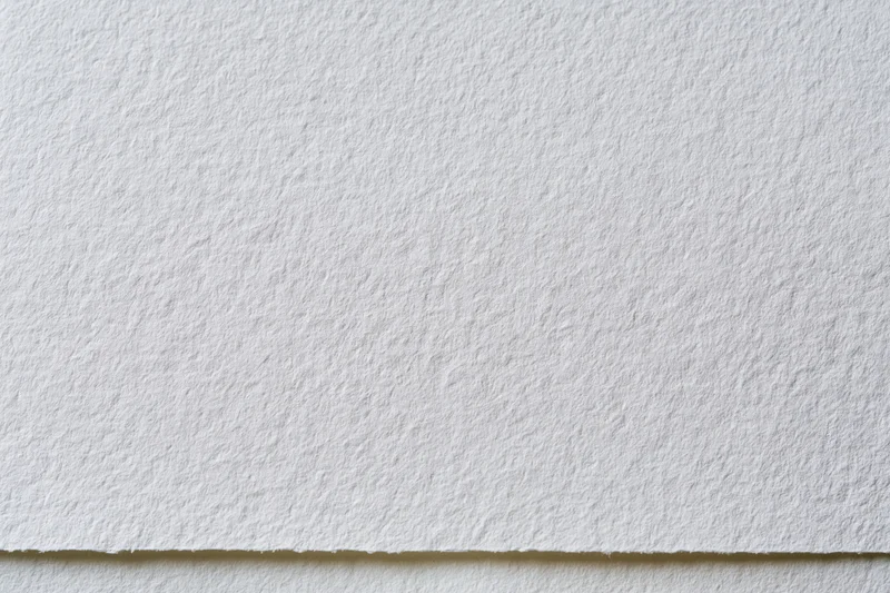 Close-up of white watercolor paper texture with visible fibers and edge detail