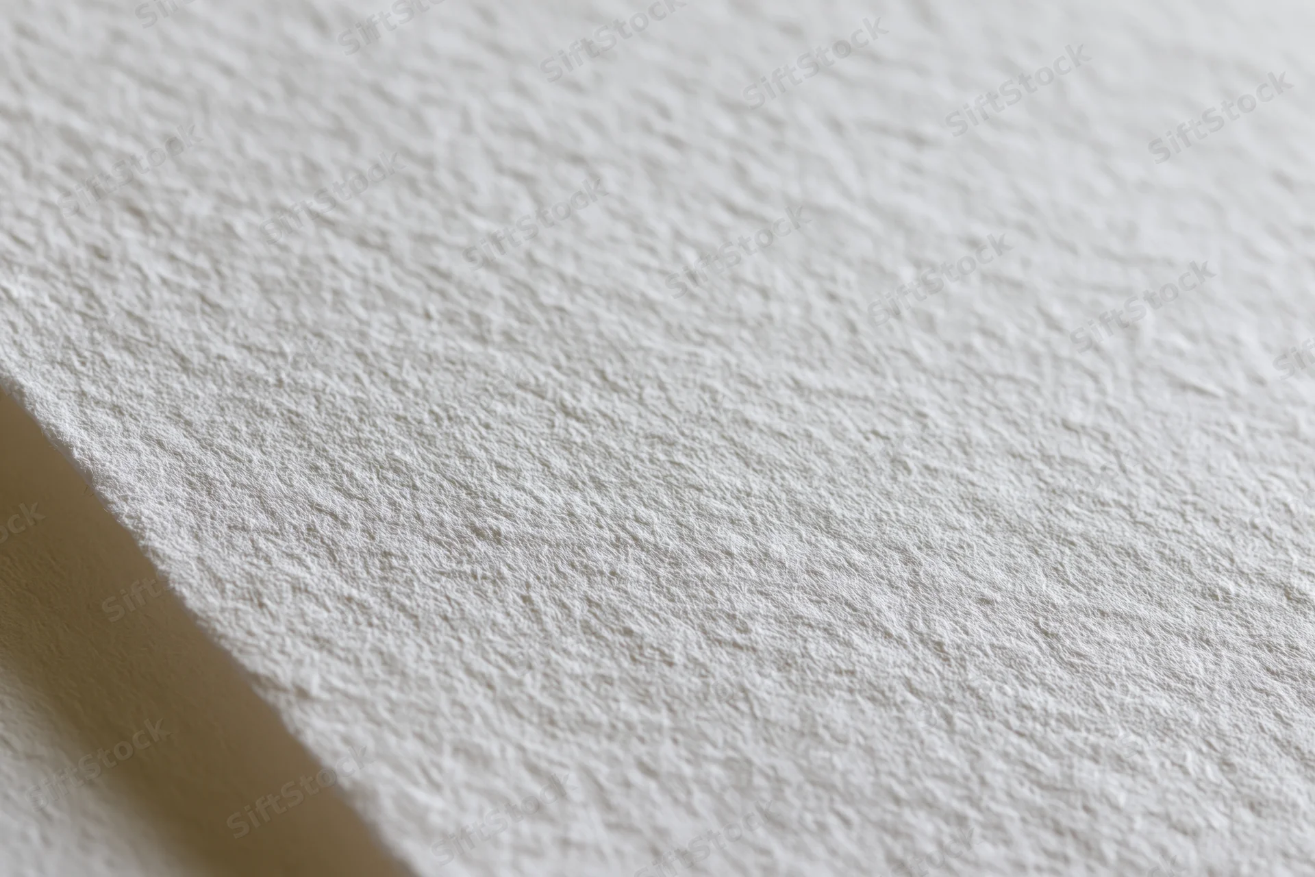 Close-up of white watercolor paper surface with textured grain and soft shadow along the edge