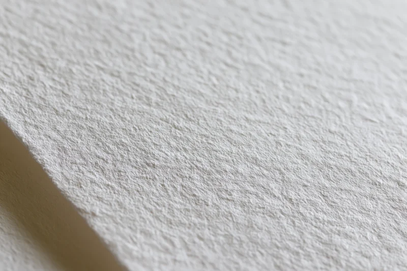 Close-up of white watercolor paper surface with textured grain and soft shadow along the edge
