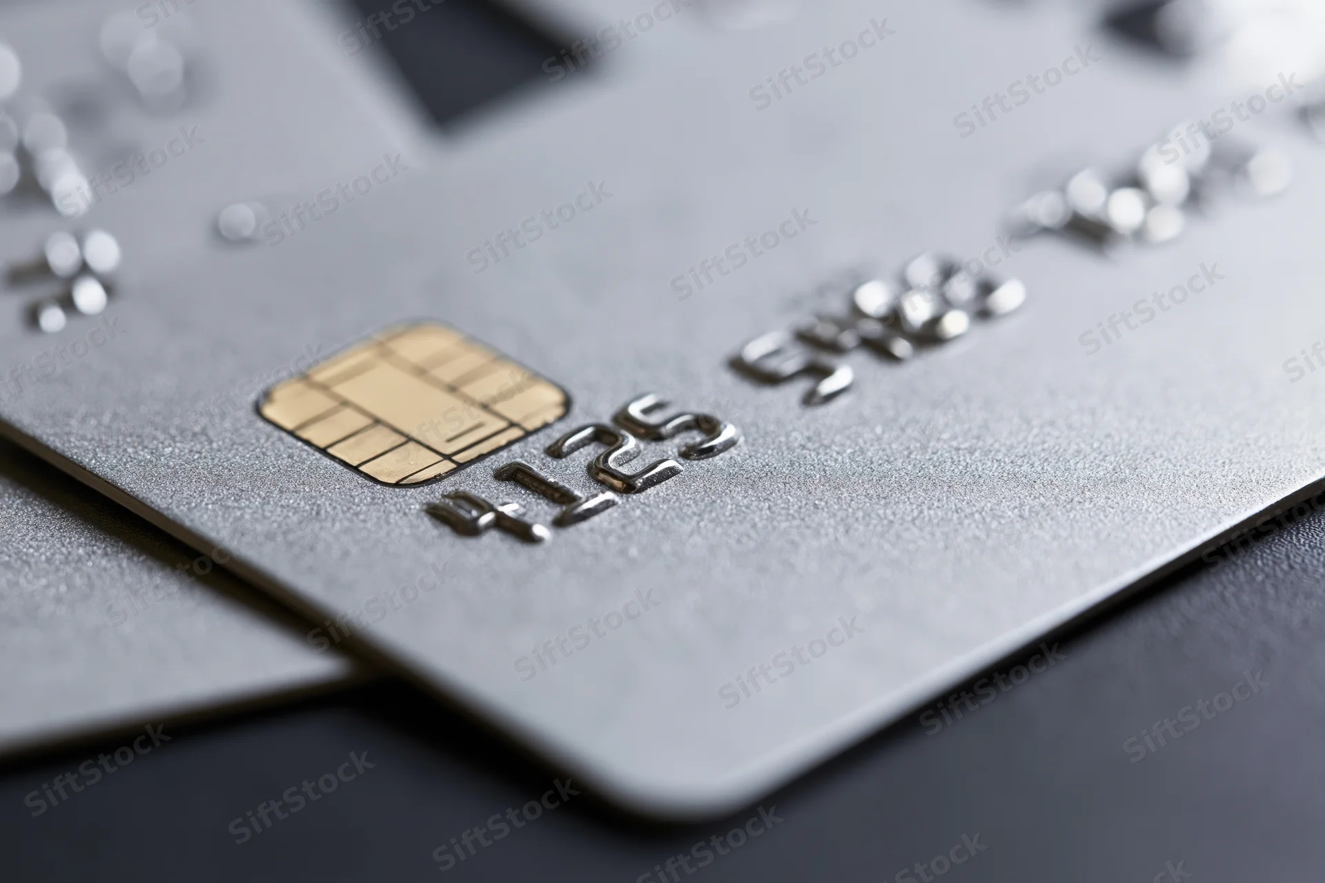 Close-up of a silver metallic credit card with embossed numbers and chip on a dark surface