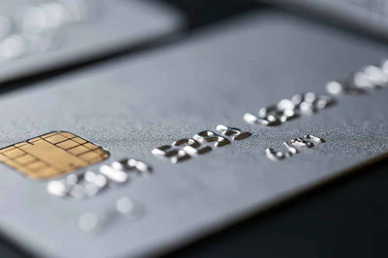 Close-up of a silver metallic credit card with embossed numbers and chip on dark surface