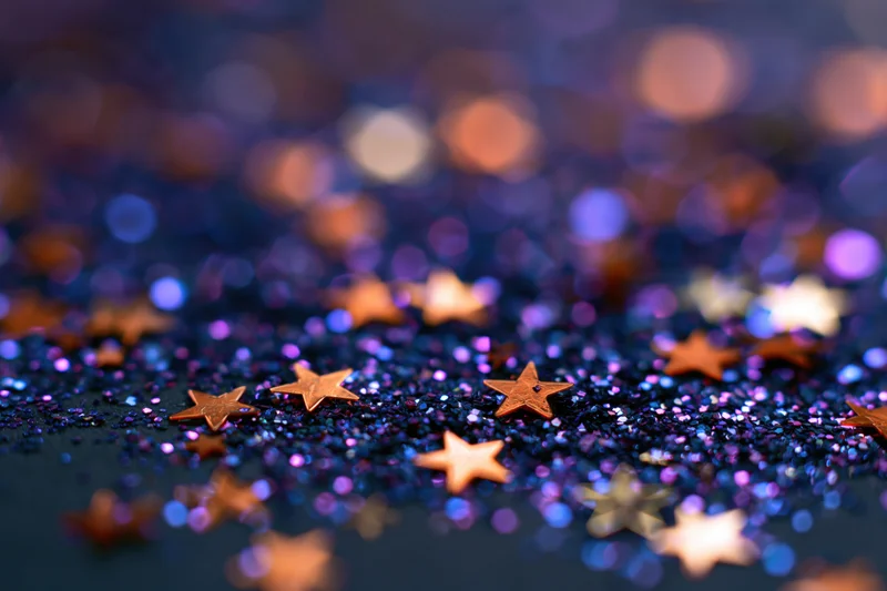 Star-shaped glitter scattered on a shimmering iridescent surface with bokeh lights in the background