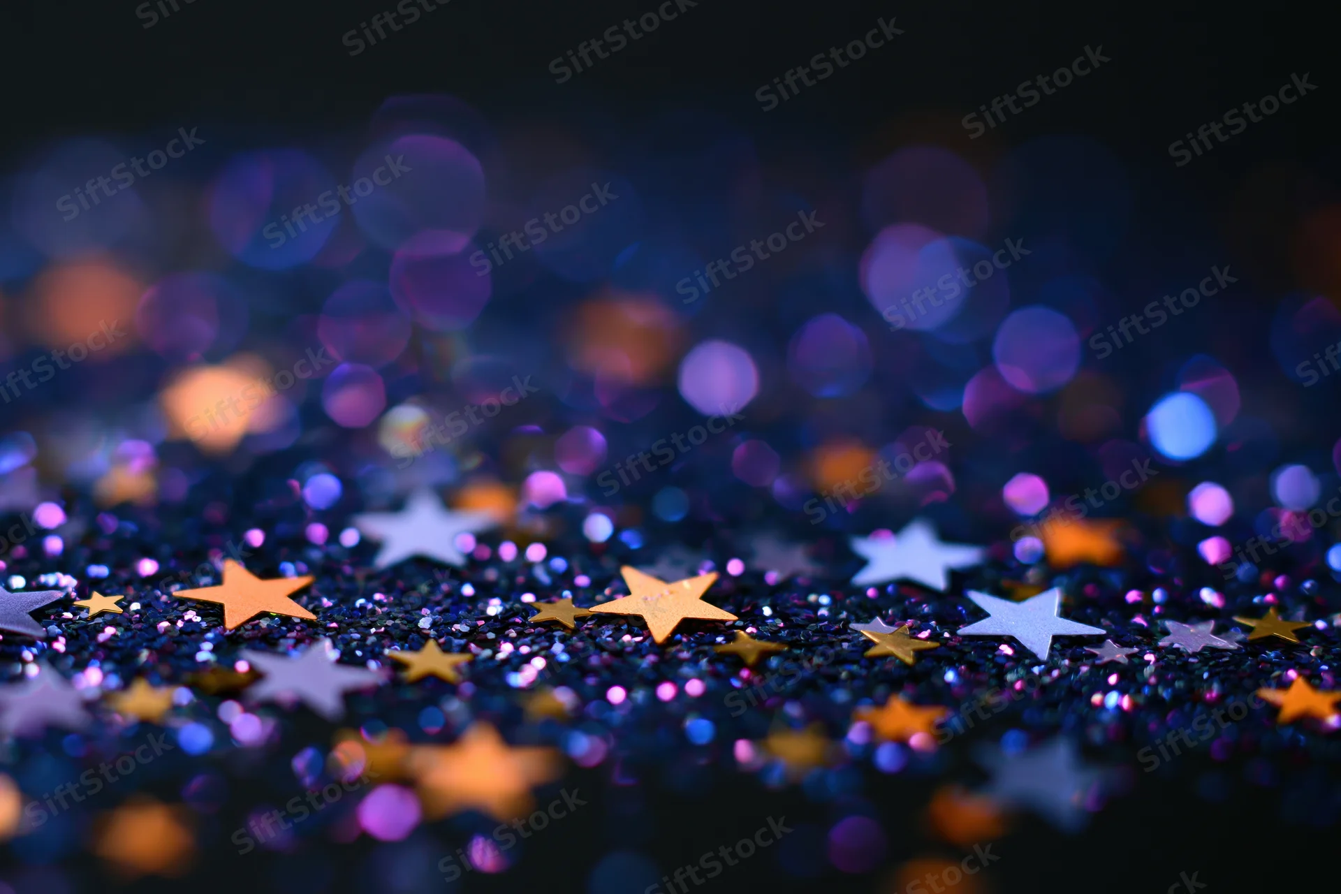 Iridescent glitter and star-shaped confetti scattered on a dark surface with bokeh lights in the background