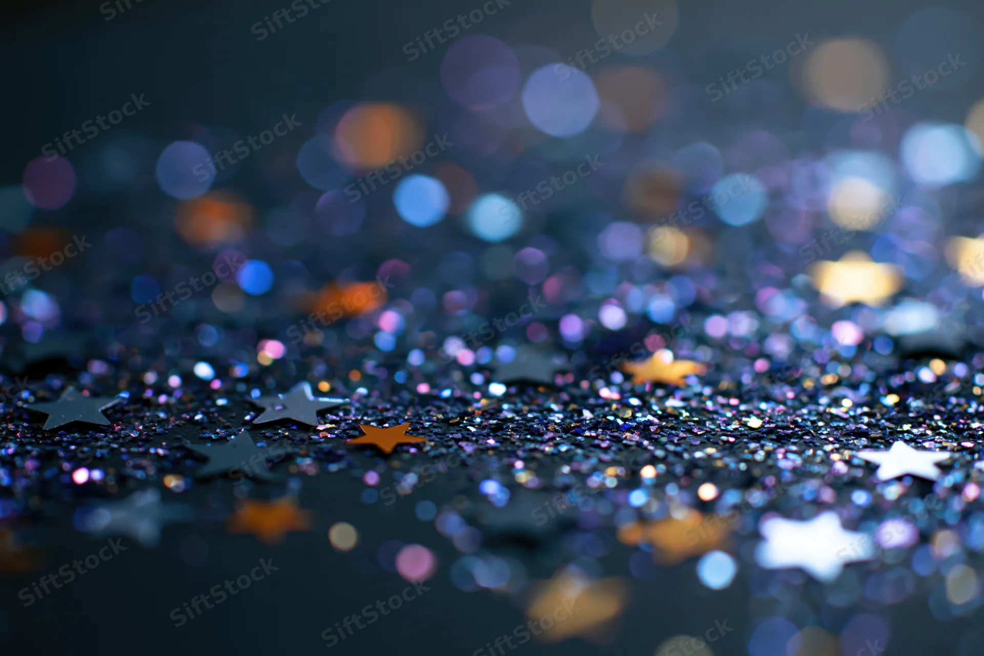 Iridescent glitter and star-shaped confetti scattered on a dark surface with bokeh lights in the background