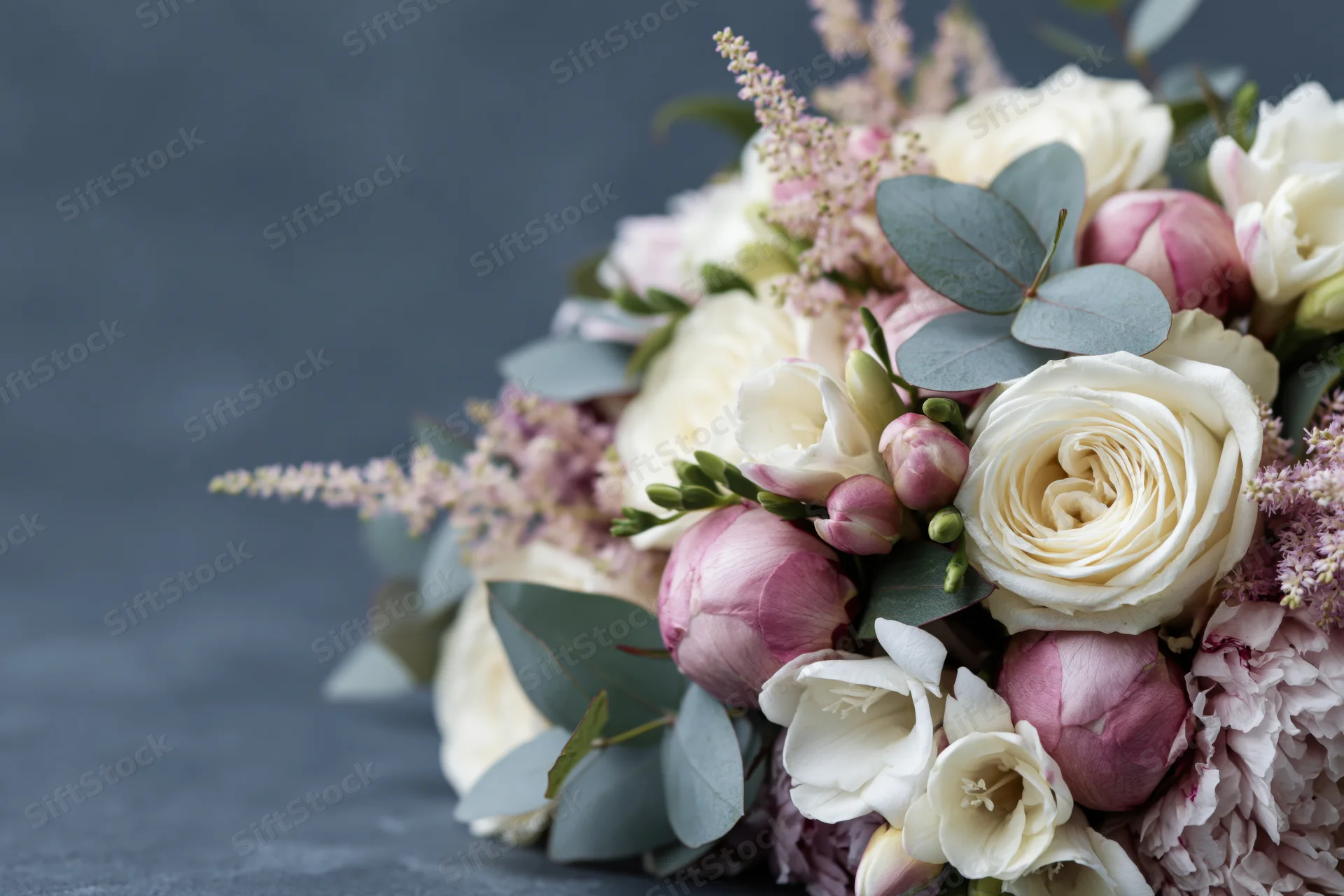 Close-up of a mixed floral bouquet with white roses, pink peonies and eucalyptus leaves on a dark surface