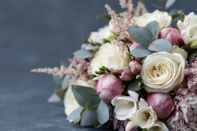 Close-up of a mixed floral bouquet with white roses, pink peonies and eucalyptus leaves on a dark surface