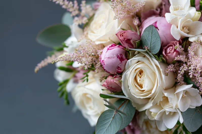 Close-up of a mixed floral bouquet with white roses, pink peonies, and eucalyptus leaves against a dark background