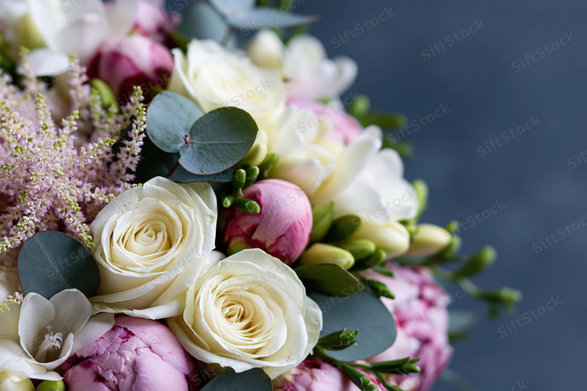 Close-up of a mixed floral bouquet with white roses, pink peonies, and green eucalyptus leaves against a dark background