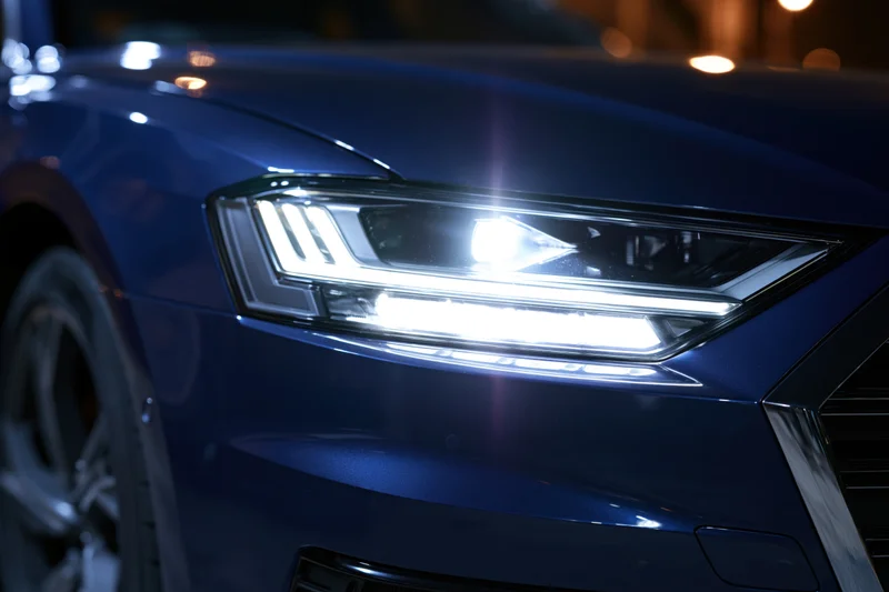 Close-up of a modern led car headlight glowing on a dark blue vehicle at night