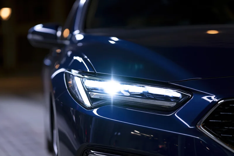 Close-up of a modern led headlight glowing on a dark blue car exterior at night