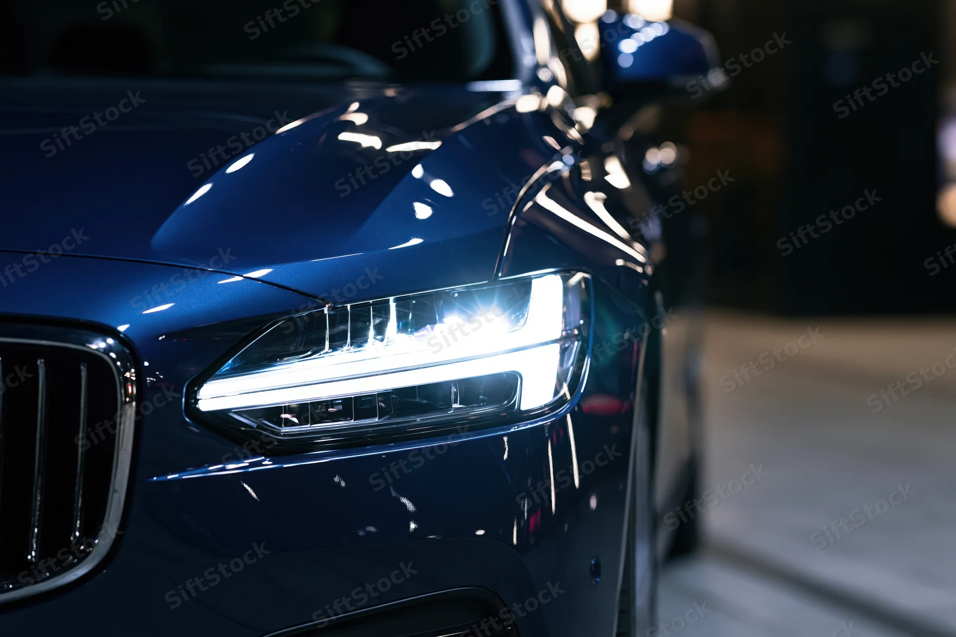 Close-up of a modern led headlight on a dark blue luxury car in a showroom
