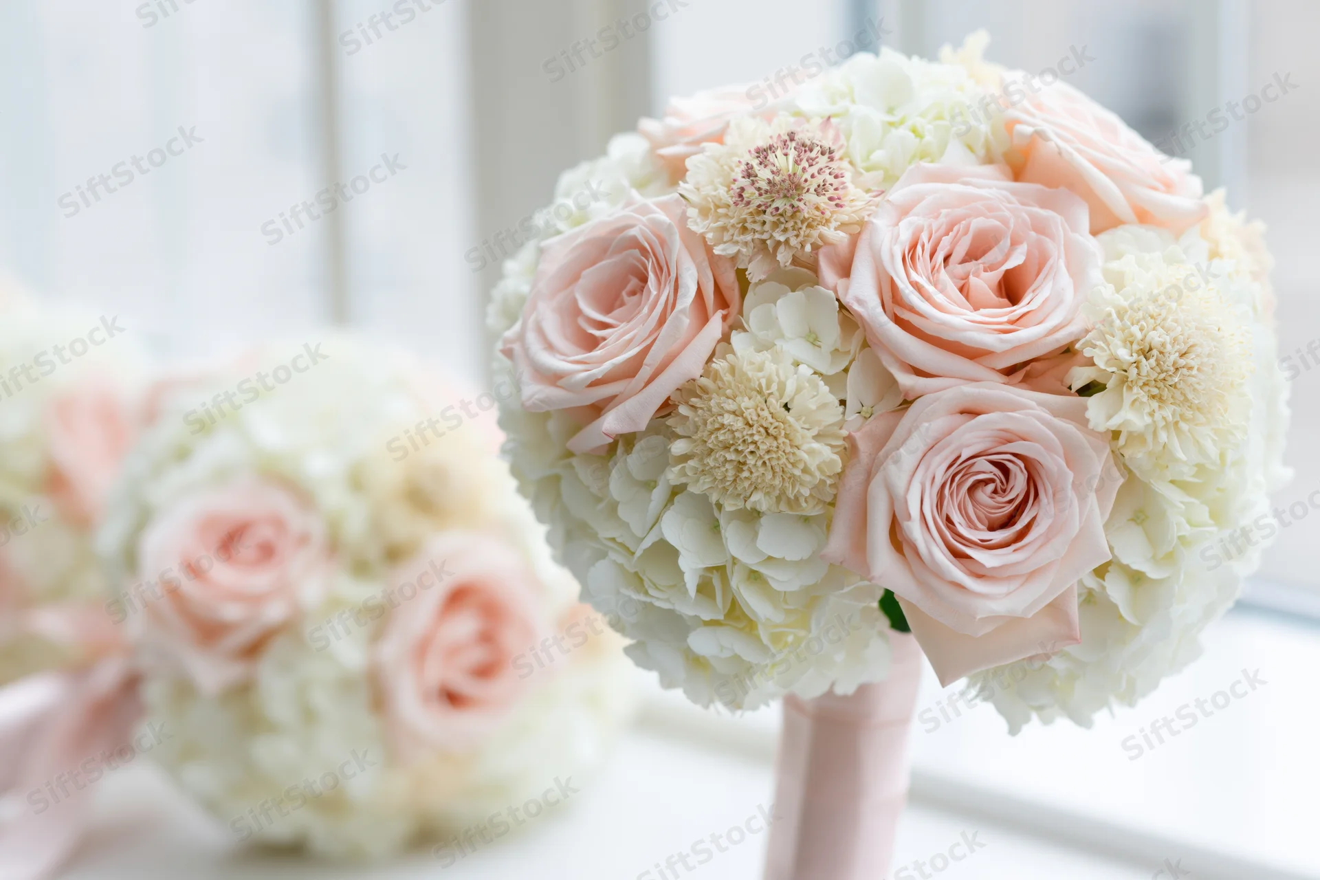 Round bridal bouquet of blush pink roses and white hydrangeas near a window