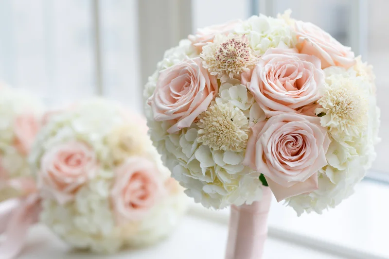 Round bridal bouquet of blush pink roses and white hydrangeas near a window