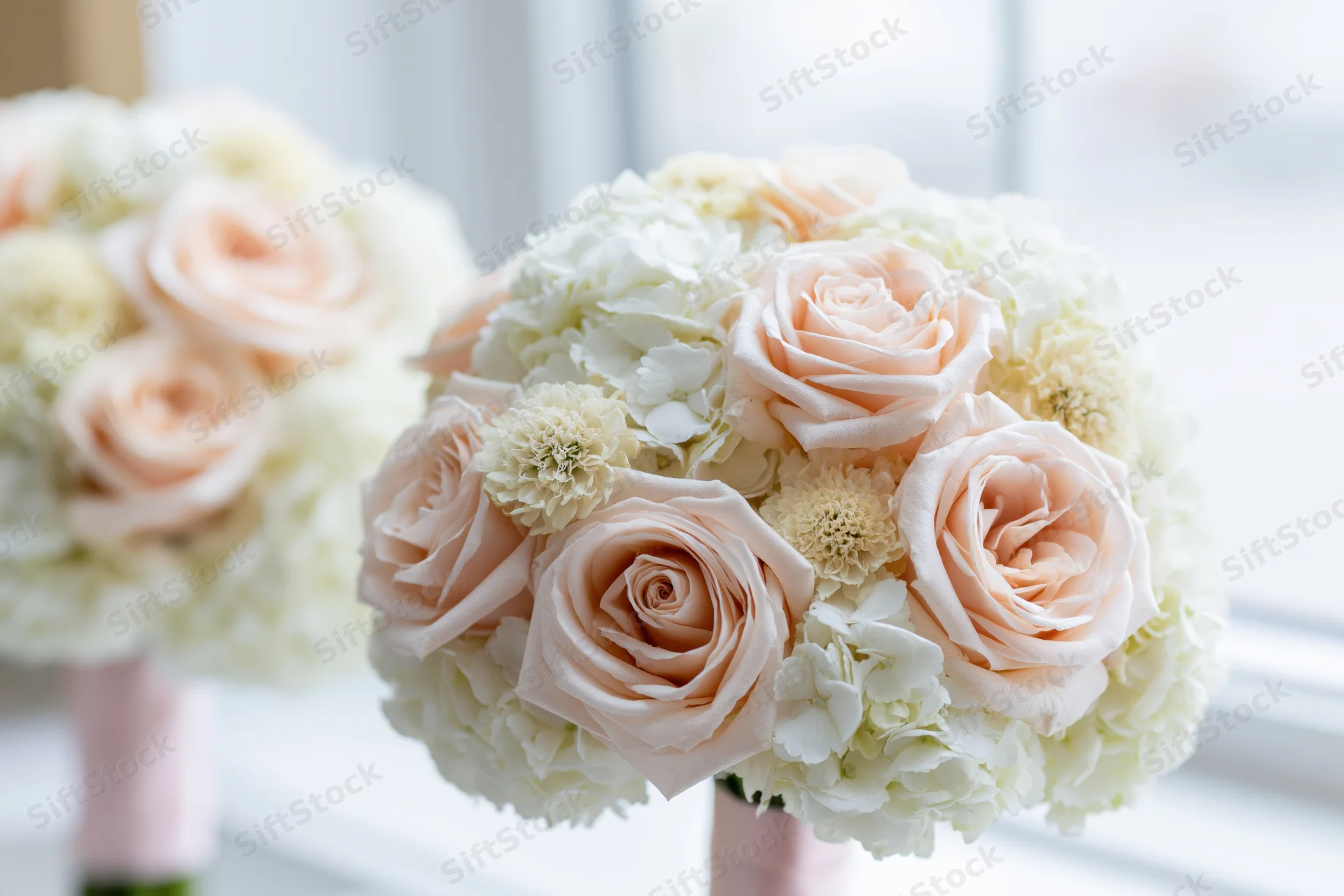 Round bridal bouquet of blush pink roses and white hydrangeas near a window