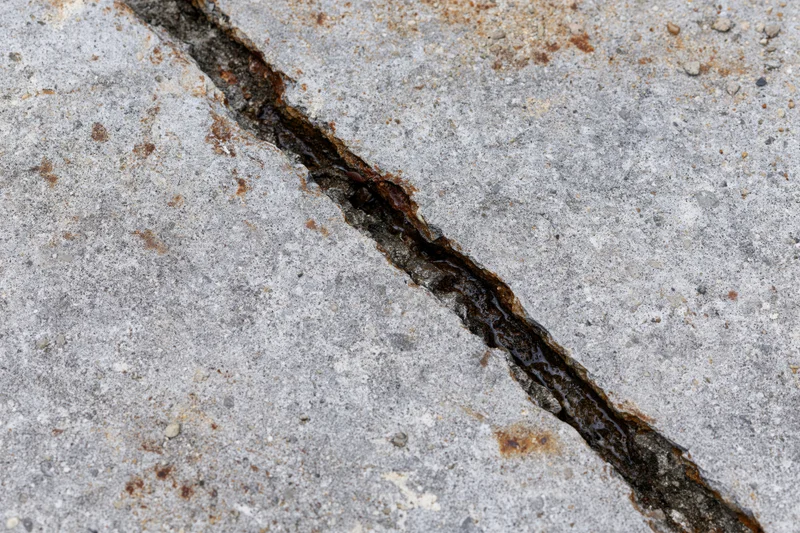 Diagonal crack in gray concrete pavement showing damage and moisture accumulation