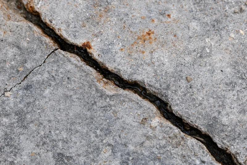 Diagonal crack in gray concrete pavement filled with black sealant