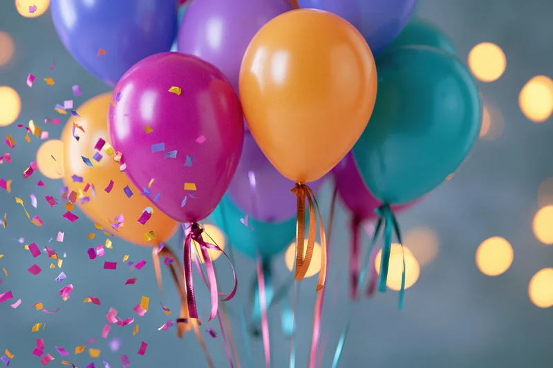 Cluster of colorful helium balloons floating with confetti and bokeh lights in the background