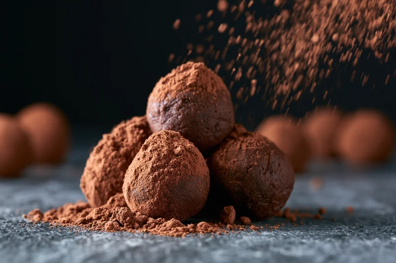 Cocoa powder dusting over a pile of chocolate truffles on a dark surface