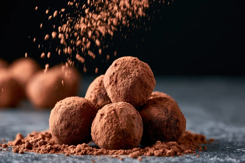 Cocoa powder falling over a pile of chocolate truffles on a dark surface